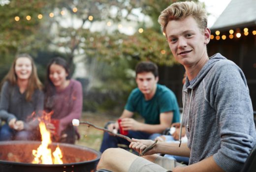Teenage boy with friends toasting marshmallow at a fire pit